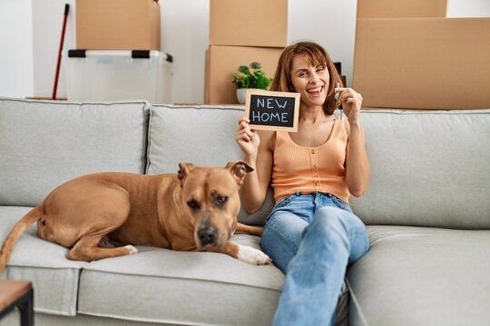Young caucasian woman holding key and new home blackboard sitting on sofa with dog at home