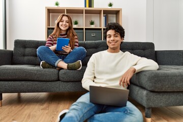 Young couple smiling happy using laptop and touchpad sitting on the sofa at home.