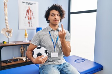 Hispanic man with curly hair working as football physiotherapist showing middle finger, impolite...