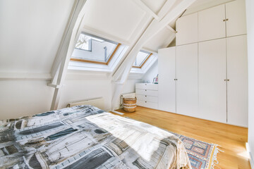 Bright attic room with a bed, windows and white wardrobes throughout the wall