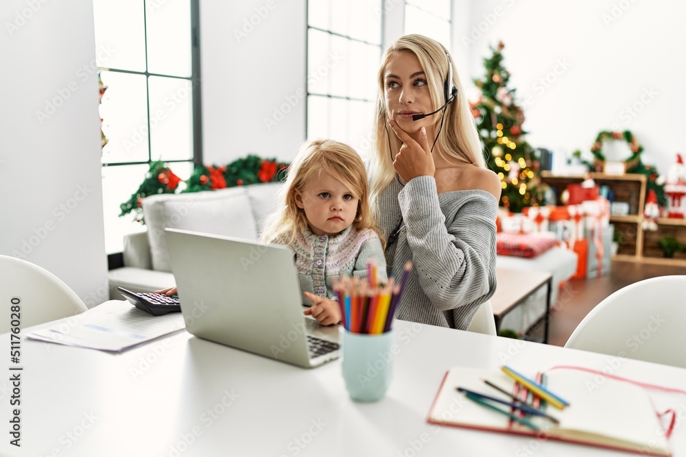 Poster Mother of caucasian daughter wearing call center agent headset at home serious face thinking about question with hand on chin, thoughtful about confusing idea