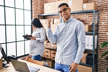 Young hispanic couple expecting a baby working at small business ecommerce pointing thumb up to the side smiling happy with open mouth