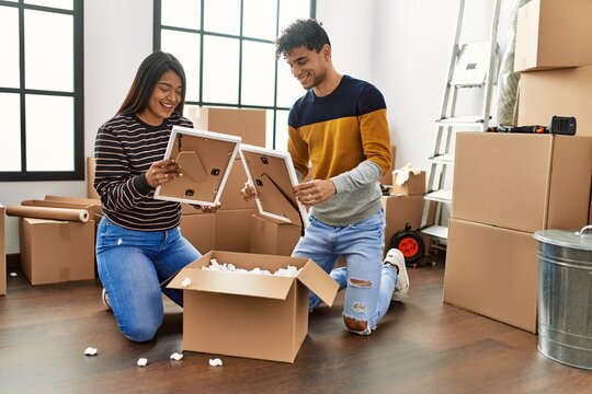 Young latin couple smiling happy unboxing cardboard box at new home.