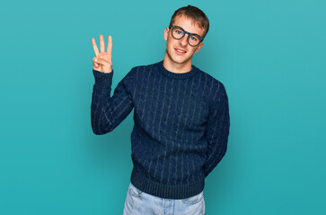 Naklejka premium Young blond man wearing casual clothes and glasses showing and pointing up with fingers number three while smiling confident and happy.