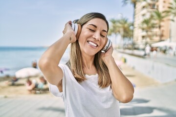 Young hispanic woman smiling confident listening to music at seaside