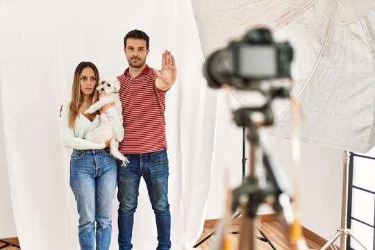 Couple of boyfriend and girlfriend with dog posing as model at photography studio with open hand doing stop sign with serious and confident expression, defense gesture