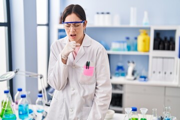 Young brunette woman working at scientist laboratory feeling unwell and coughing as symptom for cold or bronchitis. health care concept.