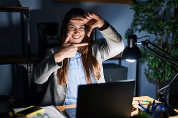 Young brunette woman working at the office at night smiling making frame with hands and fingers with happy face. creativity and photography concept.