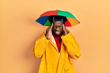 Young african american man wearing yellow raincoat with hand on head, headache because stress. suffering migraine.