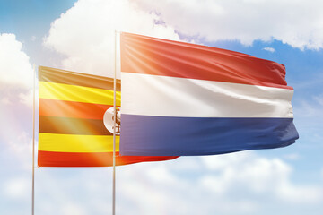 Sunny blue sky and flags of netherlands and uganda