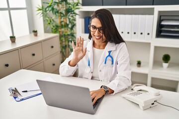 Young hispanic doctor woman doing video call at the clinic looking positive and happy standing and smiling with a confident smile showing teeth