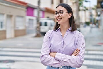 Young hispanic woman standing with relaxed expression and arms crossed gesture at street