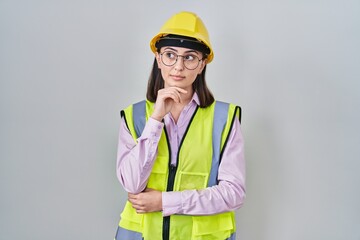 Hispanic girl wearing builder uniform and hardhat with hand on chin thinking about question, pensive expression. smiling with thoughtful face. doubt concept.