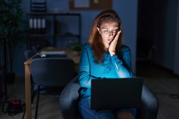 Brunette woman working at the office at night thinking looking tired and bored with depression problems with crossed arms.