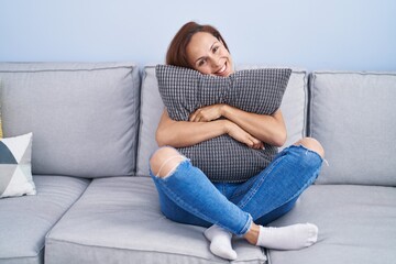 Young woman hugging cushion sitting on sofa at home