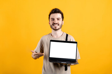 Cheerful young man wearing t-shirt posing isolated over yellow background holding laptop pc computer with blank empty screen.