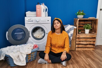 Young hispanic woman doing laundry looking sleepy and tired, exhausted for fatigue and hangover, lazy eyes in the morning.