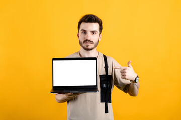 Handsome young man wearing casual clothes posing isolated over yellow background pointing with index finger to laptop pc computer with blank empty screen