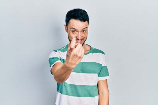 Young hispanic man wearing casual clothes beckoning come here gesture with hand inviting welcoming happy and smiling