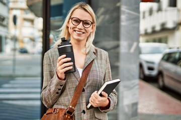 Young blonde businesswoman smiling happy drinking coffee at the city.