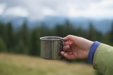 Young woman holding iron mug with hot tea at mountains background