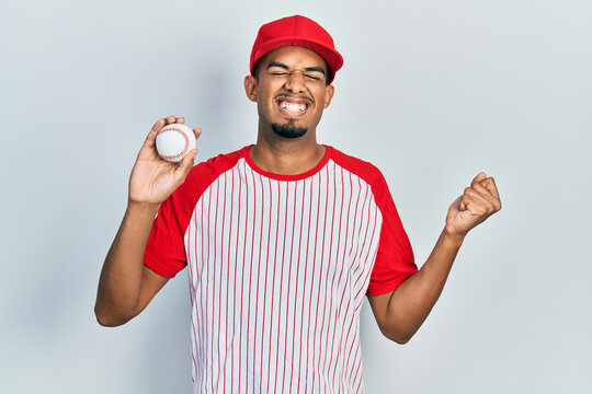 Young african american man wearing baseball uniform looking confident with smile on face, pointing oneself with fingers proud and happy.
