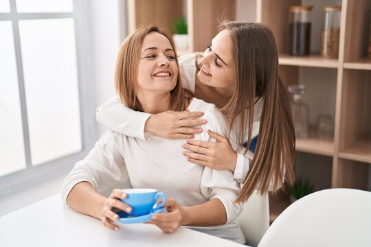 Two women mother and daughter hugging each other drinking coffee at home