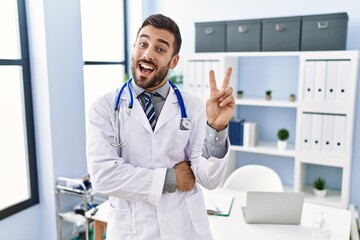 Handsome hispanic man wearing doctor uniform and stethoscope at medical clinic smiling with happy...
