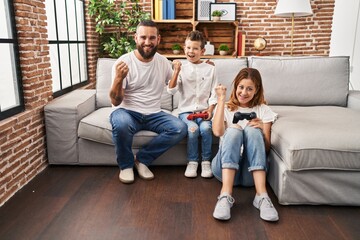 Obraz premium Family of three playing video game sitting on the sofa screaming proud, celebrating victory and success very excited with raised arms