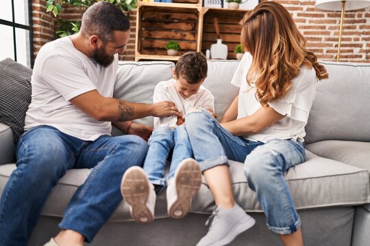 Family Doing Tickle To Son Sitting On Sofa At Home