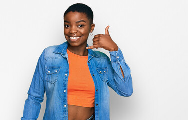 Young african american woman wearing casual clothes smiling doing phone gesture with hand and...