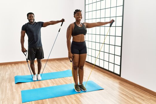 Young african american couple smiling happy training using elastic bands at home.