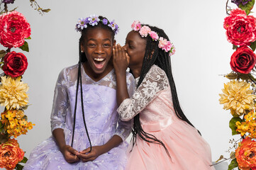 Young African-American Sisters Surrounded with Flowers Telling a Secret and Laughing