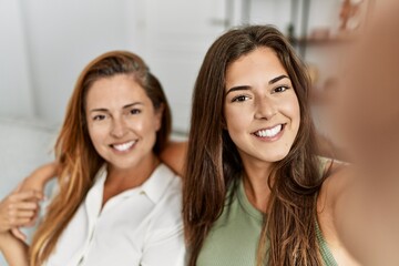 Mother and daughter smiling confident and hugging each other making selfie by the camera at home