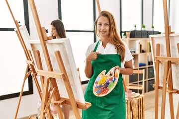 Young hispanic middle age woman at art classroom pointing finger to one self smiling happy and proud