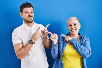 Young brazilian mother and son standing over blue background pointing aside worried and nervous...