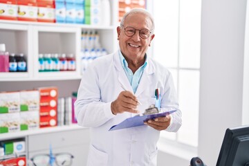 Senior grey-haired man pharmacist writing on document at pharmacy