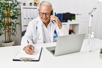 Senior man wearing doctor uniform talking on the smartphone at clinic
