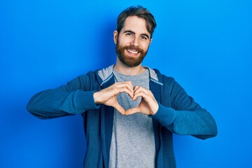 Caucasian man with beard wearing casual sweatshirt smiling in love doing heart symbol shape with hands. romantic concept.