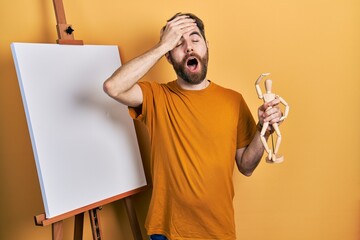 Caucasian man with beard standing by painter easel stand holding manikin stressed and frustrated...
