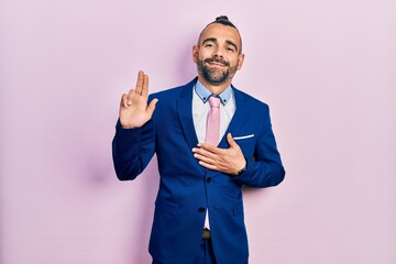 Young hispanic man wearing business suit and tie smiling swearing with hand on chest and fingers...