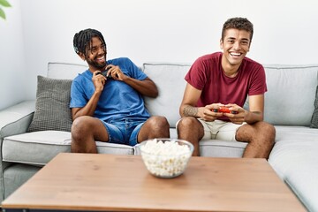 Two men friends playing video game sitting on sofa at home