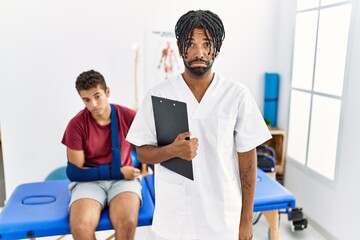 Obraz premium Young hispanic man working at pain recovery clinic with a man with broken arm depressed and worry for distress, crying angry and afraid. sad expression.