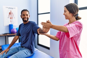 Man and woman wearing physiotherapist uniform having rehab session stretching arm at physiotherpy...