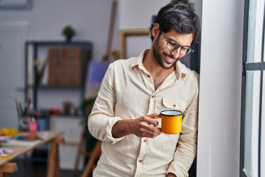 Young hispanic man artist smiling confident drinking coffee at art studio