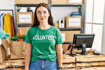 Young brunette woman wearing volunteer t shirt at donations stand smiling looking to the side and...