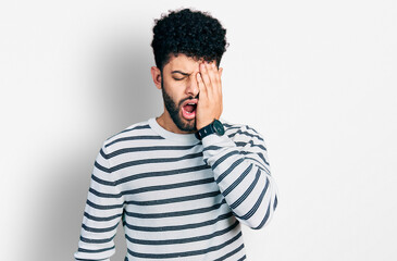 Obraz premium Young arab man with beard wearing casual striped sweater yawning tired covering half face, eye and mouth with hand. face hurts in pain.