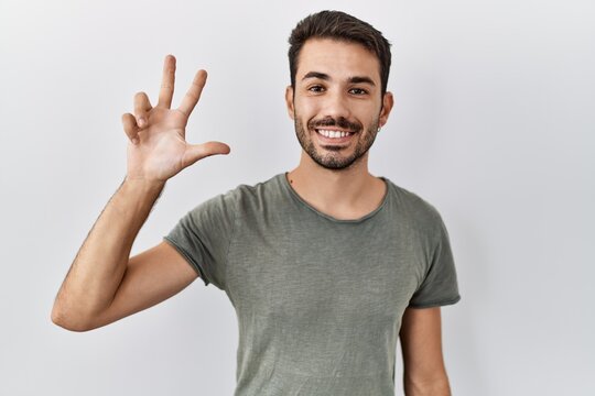 Young hispanic man with beard wearing casual t shirt over white background showing and pointing up with fingers number three while smiling confident and happy.