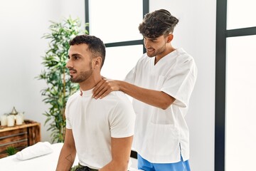 Obraz premium Two hispanic men physiotherapist and patient having rehab session massaging neck at clinic