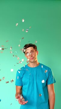 Boring party. Looser birthday. Disappointment regret. Surprise fail. Lonely celebration. Upset man feeling sad throwing confetti looking at camera isolated on green vertical copy space.
